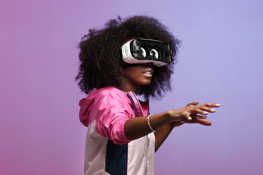 Mod young brown-haired curly girl dressed in the pink sports jacket uses the virtual reality glasses